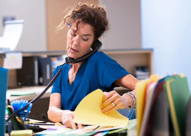 4-frontdesk healthcare worker at front desk talking on phone while sifting through papers, appearing stressed and overwhelmed